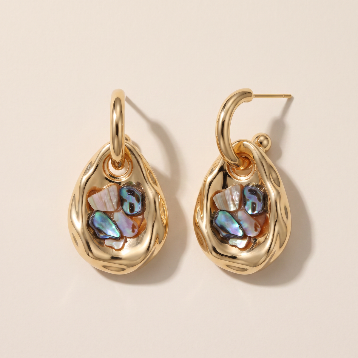 Iridescent earrings, the pair laid flat, gold hoop with a teardrop charm set with abalone shell