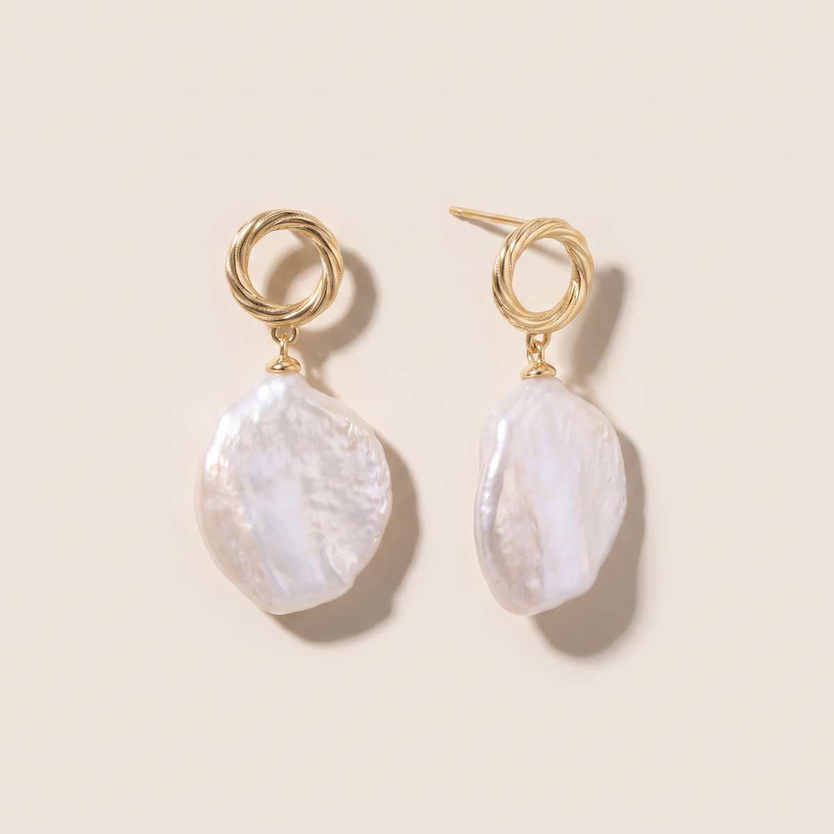 First Tide earrings, the pair laid flat, twisted gold circle with a flat baroque pearl drop