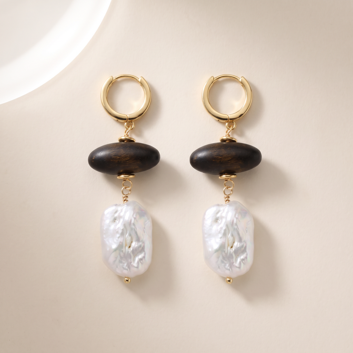 Grounded earrings, the pair laid flat, gold huggie hoop with dark wood bead and baroque pearl