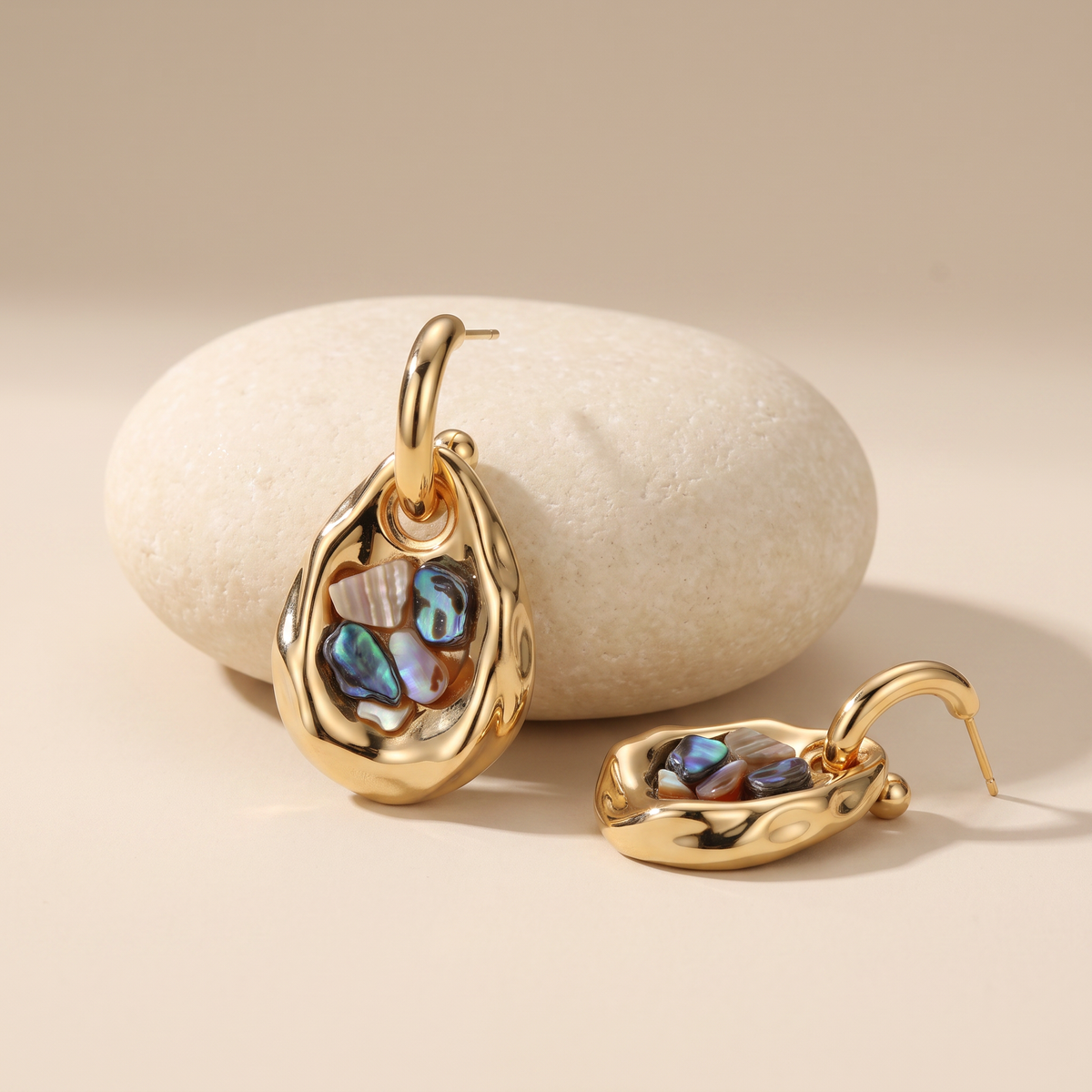 Iridescent earrings resting on a pale stone