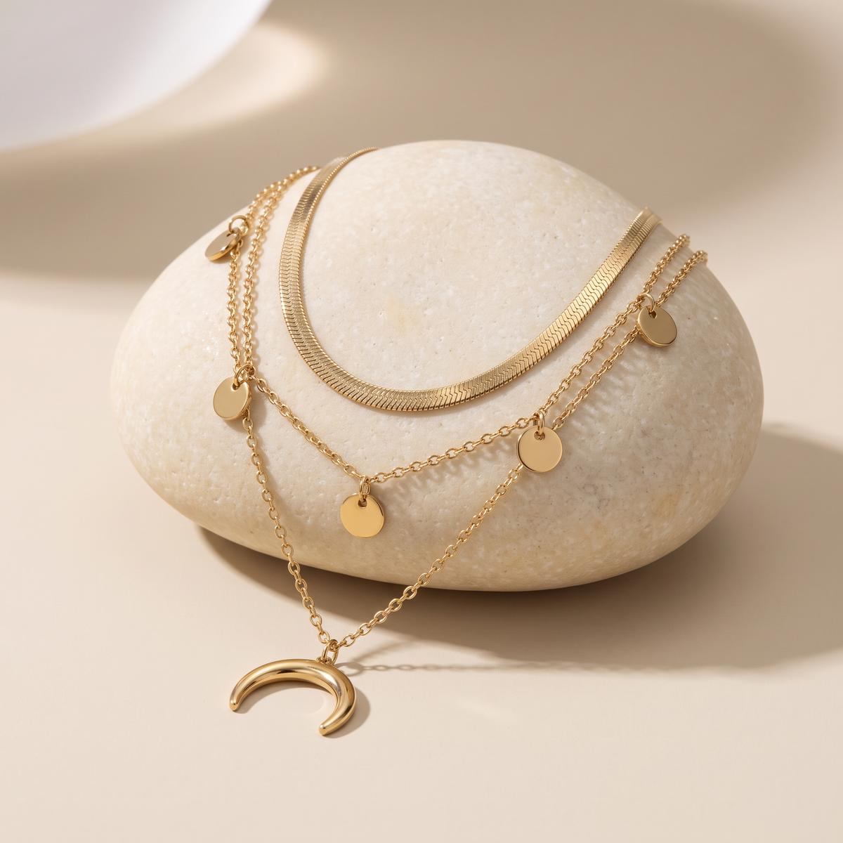 Three Moons necklace resting on a pale stone